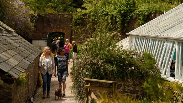 Visitors walking besides a glasshouse within a walled garden area at Greenway, Devon
